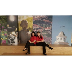 James Madison University Branch Manager Shea Baum (left) and Senior Member Service Representative Gabby Gill pose on in-branch bleacher seating in front of the JMU mural wall.