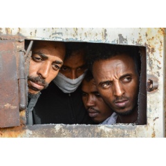 Men look out of an opening in the main gate of a warehouse in Zintan detention center, south of Tripoli, where 700 people are being detained. LIBYA 2019  Jrme Tubiana/MSF