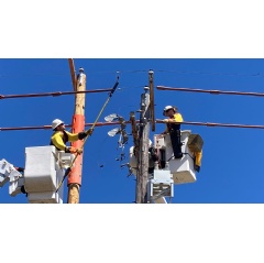 A photo of line workers installing cross arms on a utility pole