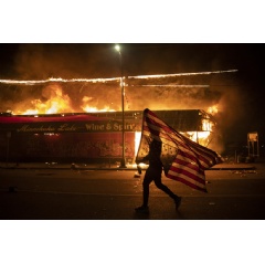 A protester carries a U.S. flag upside down, a sign of distress, next to a burning building, May 28, 2020, in Minneapolis. (AP Photo/Julio Cortez)