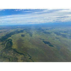Aerial view of Alaska out the window of a NASA Gulfstream III plane. The land is mostly lush and green, with lakes dotting it and rivers snaking through the landscape. The sky is blue and has puffy white clouds. Credit: NASA / Sofie Bates